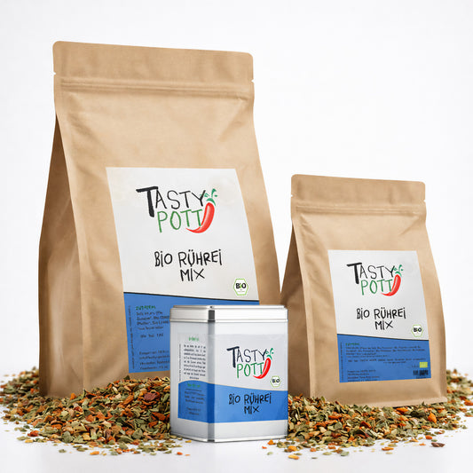 Tasty Pott Bio Rührei Mix Gewürzmischung im braunen Nachfüllbeutel und in einer Dose, umgeben von bunter Gewürzmischung, frontal fotografiert.
