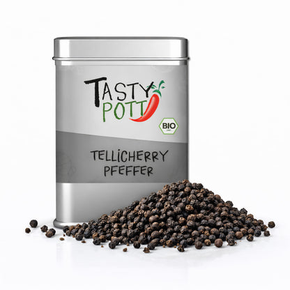 Tasty Pott Tellicherry Pfeffer ganz in silberner Dose, davor ein Haufen ganzer schwarzer Pfefferkörner auf weißem Untergrund.