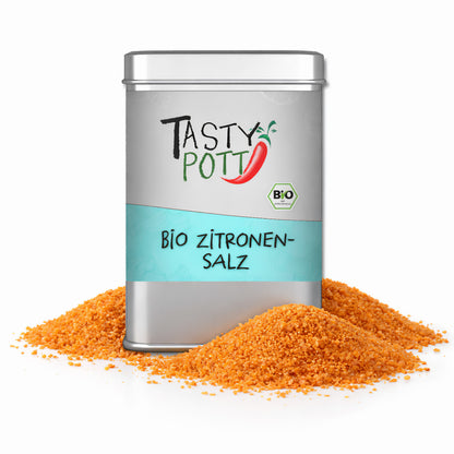 Tasty Pott Bio Zitronensalz in silberner Dose, umgeben von zwei Häufchen gelbem Zitronensalz-Granulat.