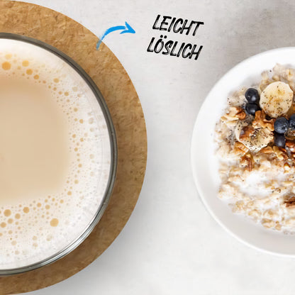 Ein Glas angerührter veganer Haferdrink neben einer Schale Porridge mit Früchten, Hinweis auf leichte Löslichkeit des Pulvers.
