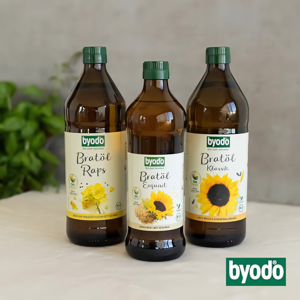 Drei Flaschen Byodo Bratöl nebeneinander, darunter Bratöl Raps, Bratöl Exquisit und Bratöl Klassik mit Sonnenblume, auf hellem Tisch.