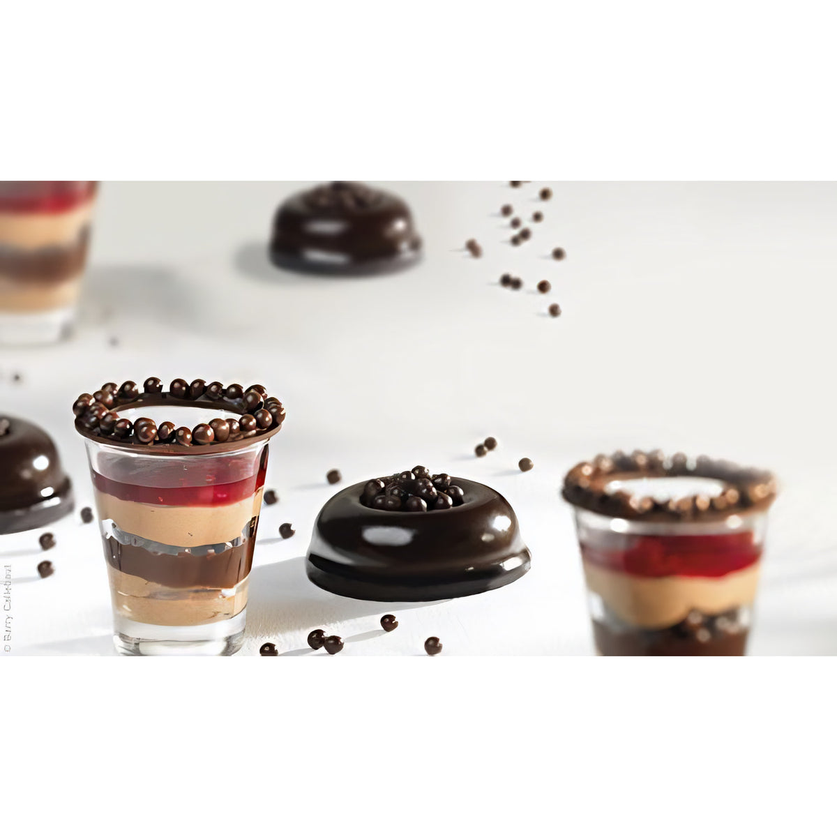 Dessert im Glas und Gebäck mit dunklen Callebaut Crispearls Müslibällchen als Dekoration auf weißem Untergrund.