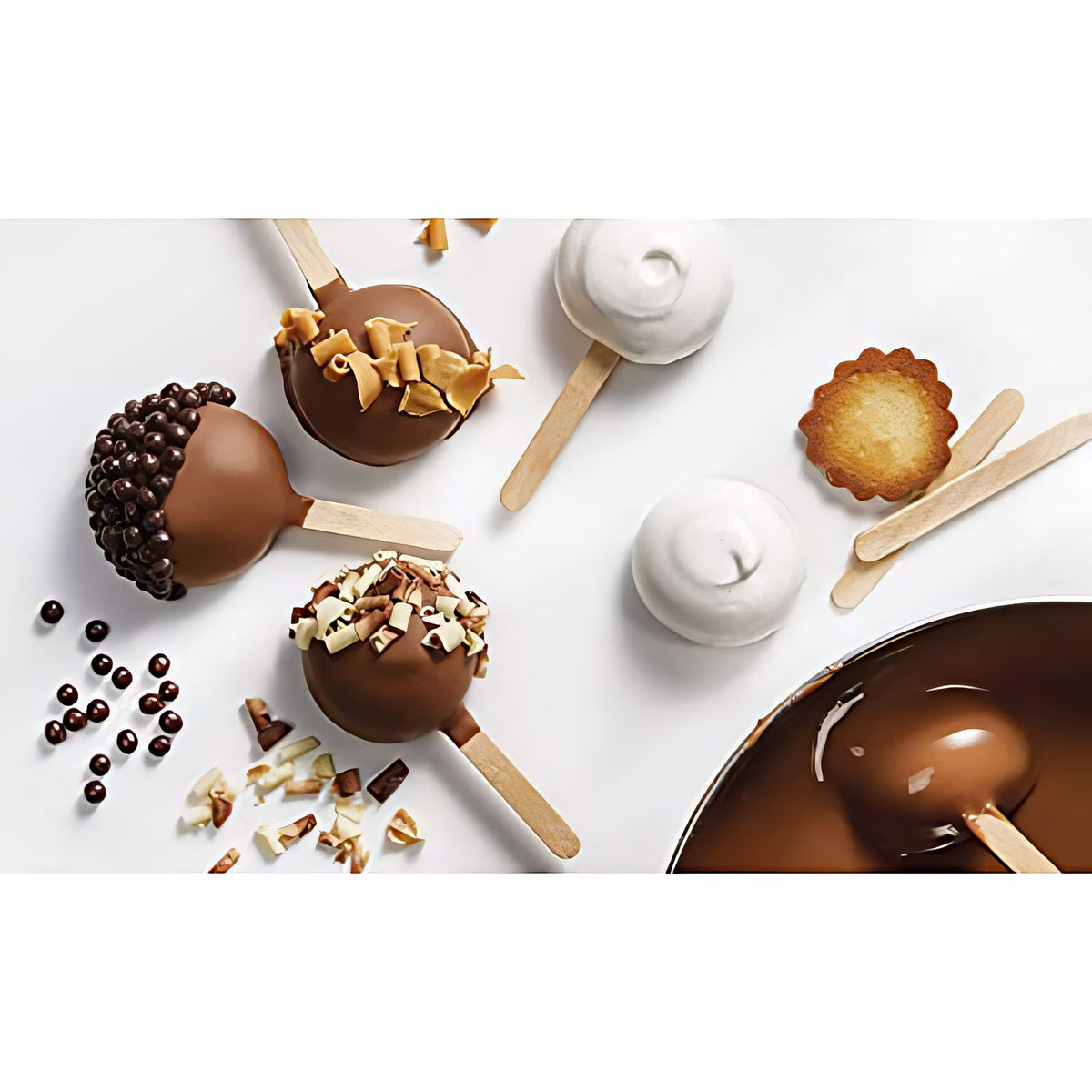 Mit Schokolade überzogene Cake Pops, teilweise mit Mona Lisa Crispearls dekoriert, daneben lose Müslibällchen und Backzutaten.