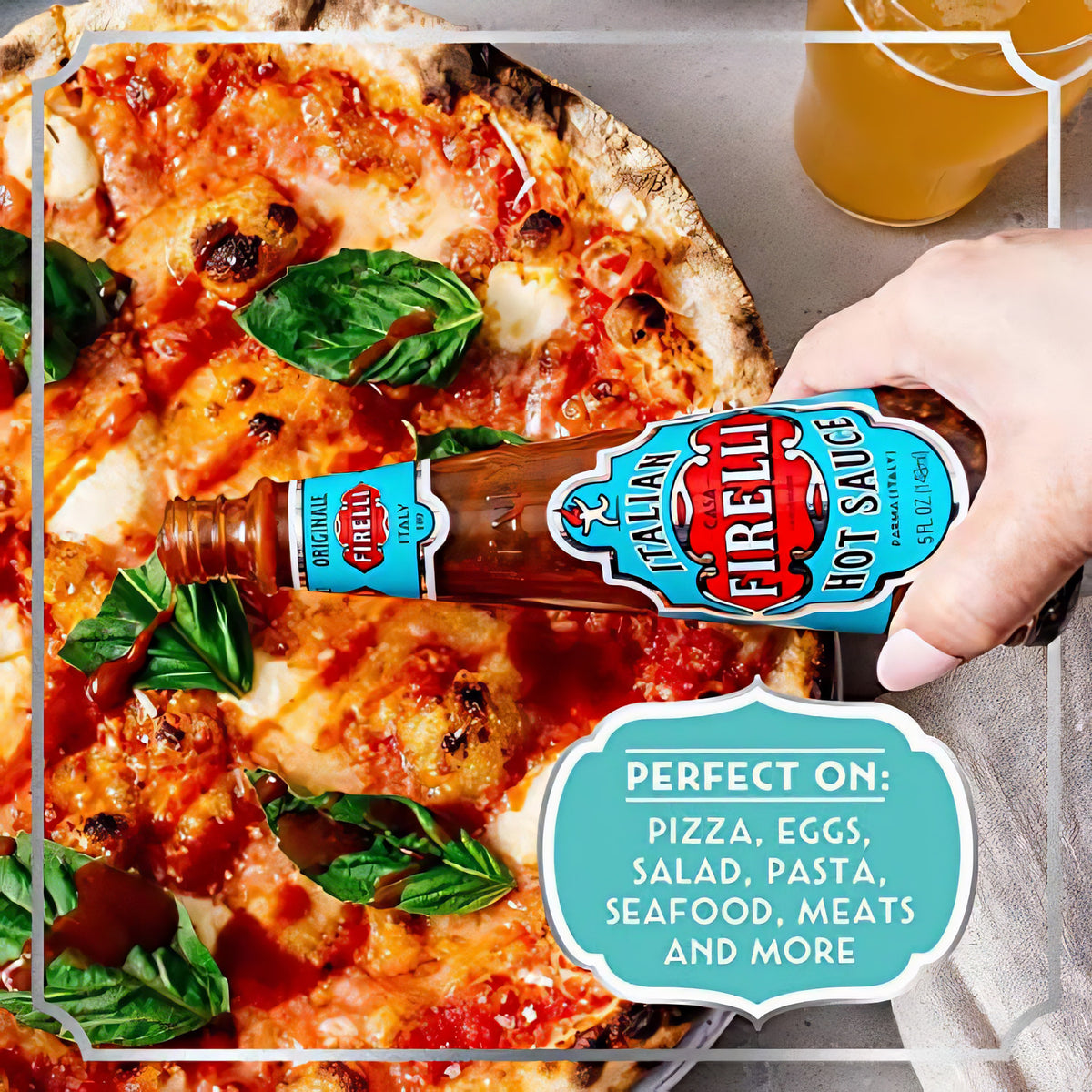 Hand hält eine Glasflasche Firelli Sauce und gibt sie als pikantes Topping auf eine Pizza mit Basilikum.