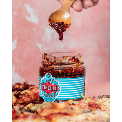 Casa Firelli Chili Crunch Glas, ein Holzlöffel mit Chili Crunch wird über Pizza gehalten.