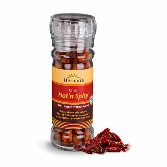 Herbaria Glasmühle mit ganzen getrockneten spicy Chilis, daneben einige lose Chilischoten auf weißem Hintergrund.