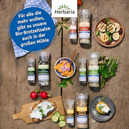 Verschiedene Herbaria Brotzeitsalz Mini-Mühlen und große Mühlen mit weiteren Gewürzmischungen, arrangiert auf einem Holztisch mit Brotzeit und frischen Kräutern.