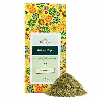 Herbaria Grüner Hafer Kräutertee in gelber, bunt gemusterter Verpackung mit losem, grünem Haferkraut davor auf weißem Hintergrund.