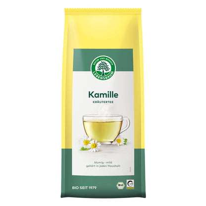 Lose Kamille von Lebensbaum in gelber Tüte, vorne ein Glas mit hellem Kräutertee und Kamillenblüten, Produkt von vorne gezeigt.