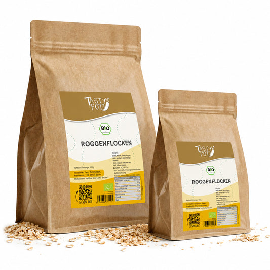 Zwei Beutel tasty pott Bio Roggenflocken aus braunem Kraftpapier, stehend auf einer Holzoberfläche mit verstreuten Roggenflocken, Vorderseiten mit Etikett sichtbar.