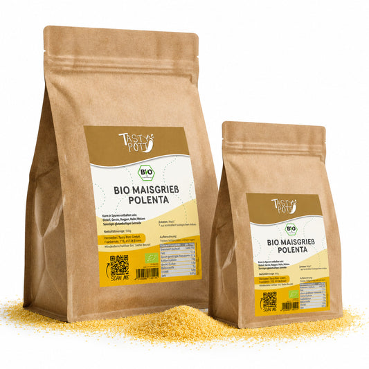 Zwei braune Beutel Tasty Pott Bio Maisgrieß Polenta mit Sicht auf Etikett, stehend auf verstreutem Maisgrieß.