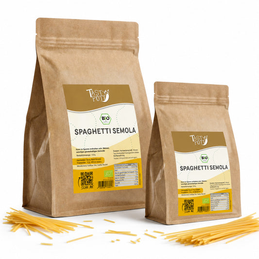 Zwei braune Beutel Tasty Pott Bio Spaghetti Semola mit Sichtfenster auf die Verpackung und lose Spaghetti-Nudeln im Vordergrund.