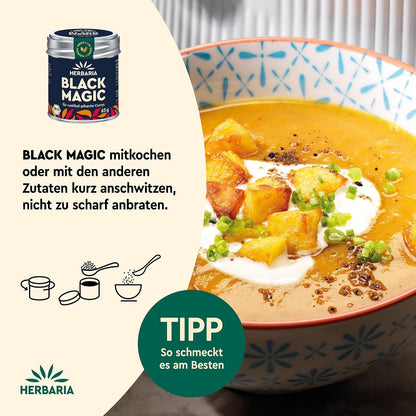 Schale mit cremigem Currygericht, garniert mit gebratenen Kartoffelwürfeln und Kräutern, daneben Herbaria Black Magic Curry Gewürzmischung.