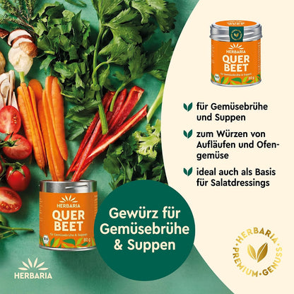 Herbaria Querbeet Gewürze-Dose neben frischem Gemüse wie Karotten, Sellerie und Tomaten auf grünem Untergrund