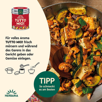 Gebratene Pilze, Zucchini und Käse in einer Pfanne, daneben Herbaria Tutto Mio Dose und Anwendungstipp für das Gewürz während des Garens.