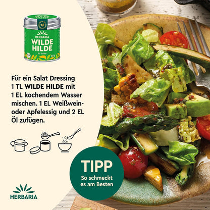 Teller mit gemischtem Salat, Avocado, Tomaten und Mais, daneben Herbaria Wilde Hilde Dose und Zubereitungstipp für Salatdressing.