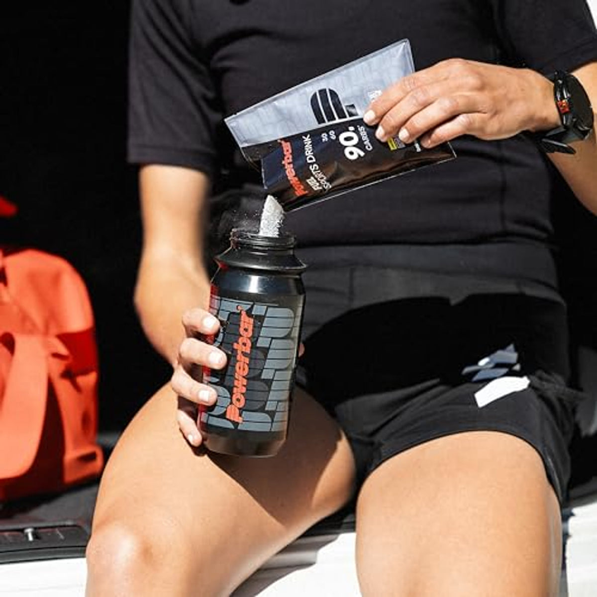 Person füllt Powerbar Black Line Fuel 90 High Carb Sports Drink Pulver aus einem Beutel in eine schwarze Powerbar-Trinkflasche.